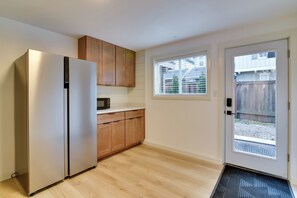 A compact kitchen with a refrigerator, wooden cabinets, a microwave, and a window with blinds. - Healthcare Workers' Home Base! Portland Apt (Portland)