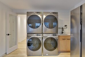 Ein Waschraum mit vier übereinandergestapelten Waschmaschinen mit Frontlader, einem Waschbecken und einem Holzkasten.