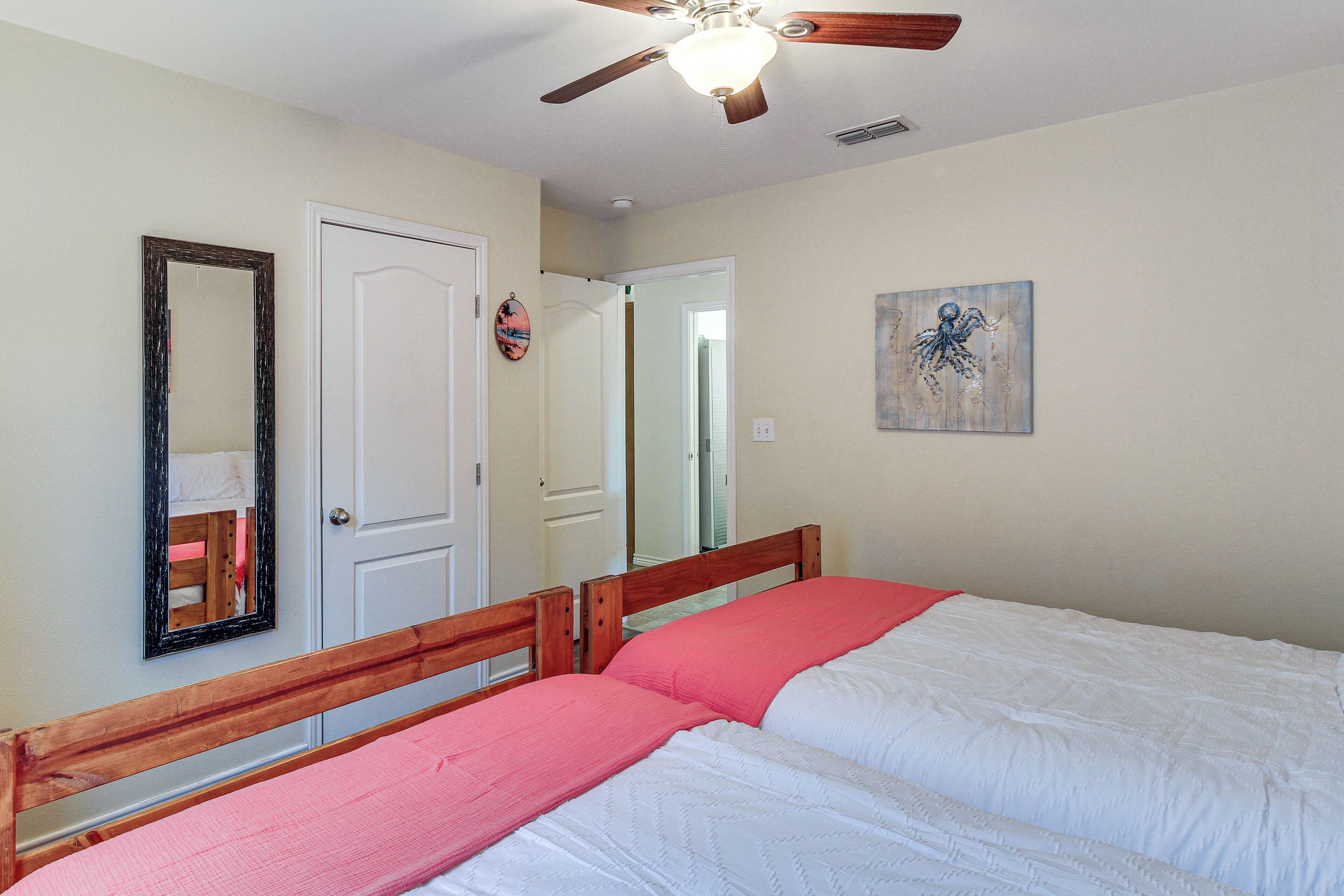 A bedroom with a wooden bed, a ceiling fan, a white door, and a wall-mounted mirror.