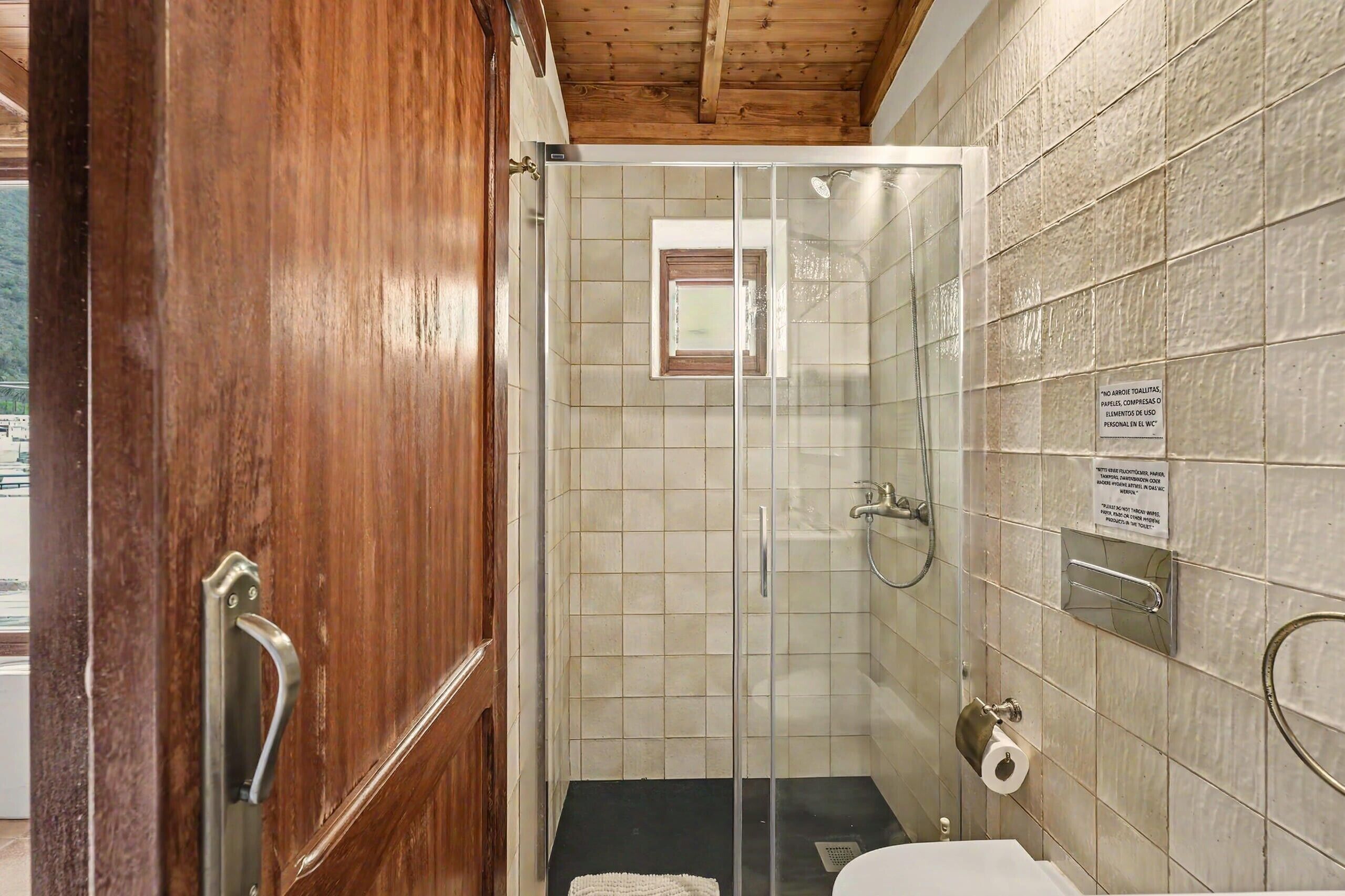 Une douche avec une porte en verre, une serviette et un panneau sur le mur.