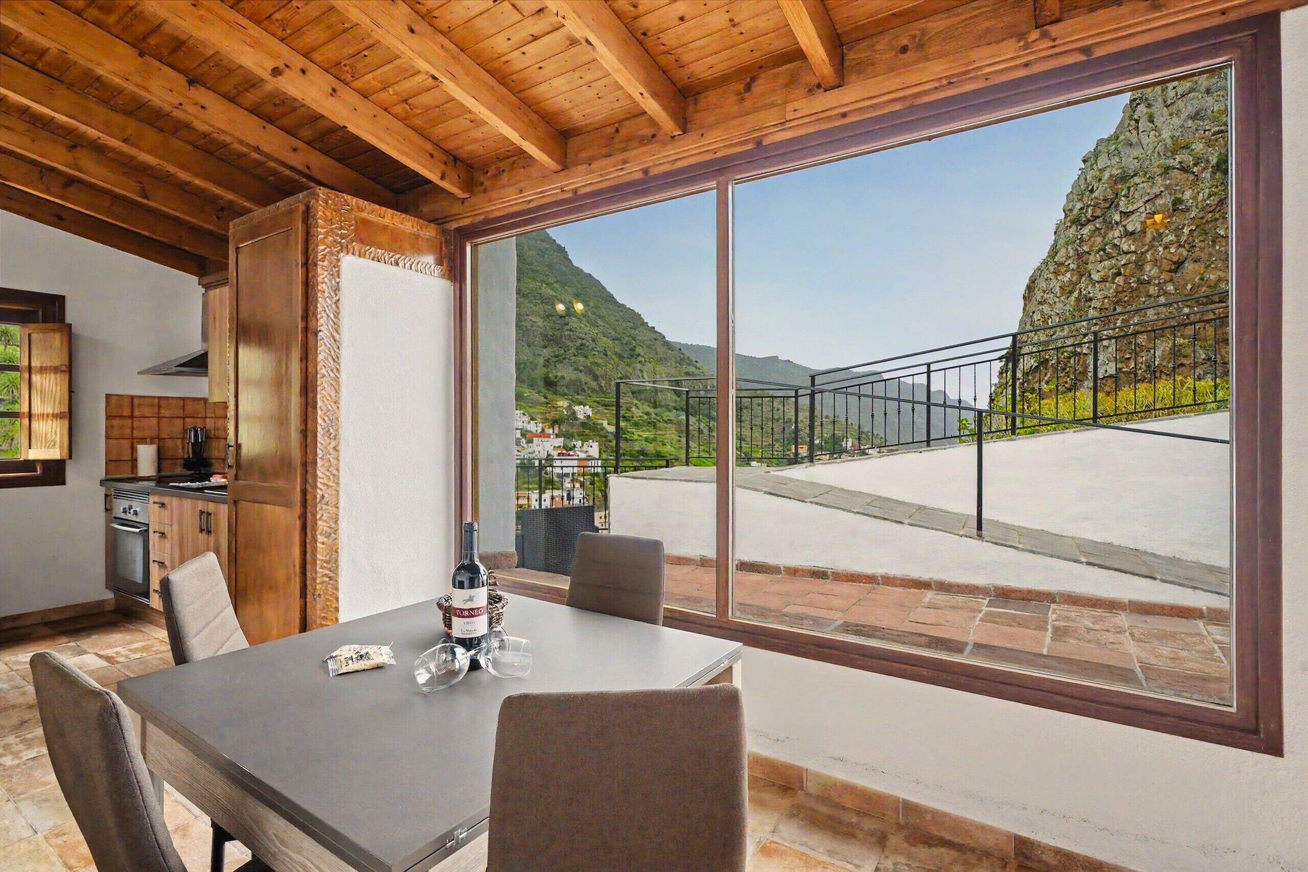 Ein Essbereich mit Tisch, Stühlen und Blick auf eine gebirgige Landschaft durch große Fenster.