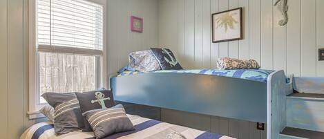 Un dormitorio con una cama nido, una ventana con persianas, un cuadro enmarcado y un adorno con forma de caballito de mar en la pared.