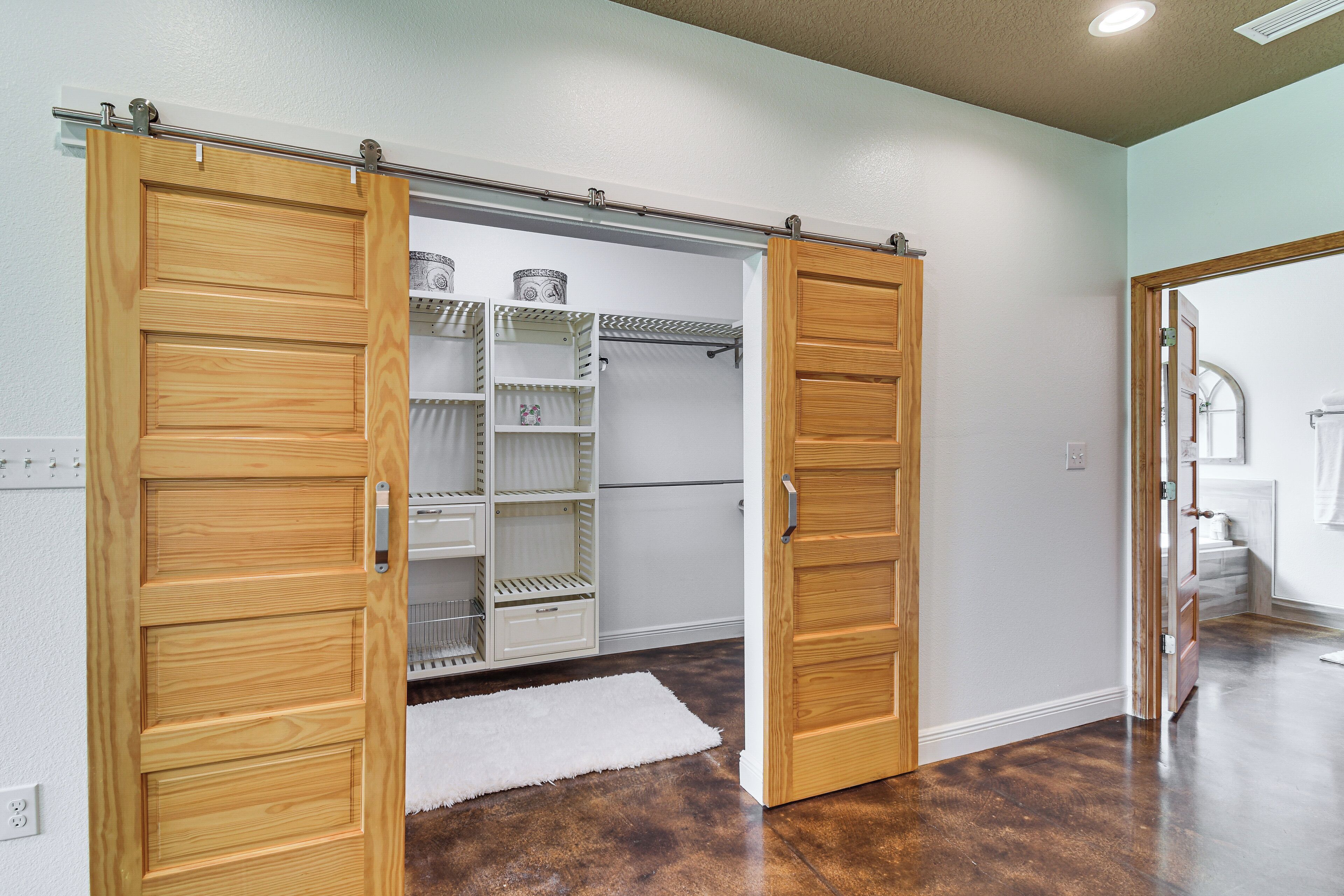 A room with a wooden sliding door, a white closet with shelves, and a white rug on the floor.