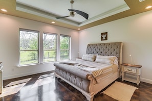 A bedroom with a large bed, a ceiling fan, and three windows.