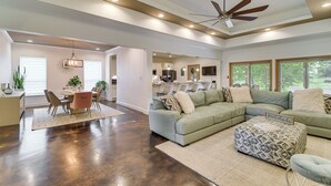 A spacious living area with a large sectional sofa, a dining table with chairs, a ceiling fan, recessed lighting, and a kitchen in the background. - Elegant Home w/ Outdoor Kitchen in Robertsdale (Robertsdale)