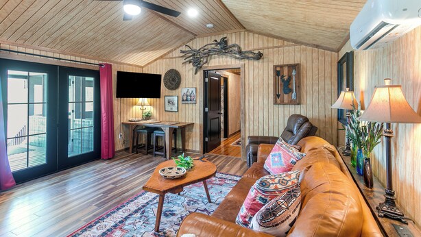 A spacious living room with a wooden ceiling, a ceiling fan, a leather sofa, a dining table, and a large window. - Couple's Retreat, Hunter's Home Base (Enigma)