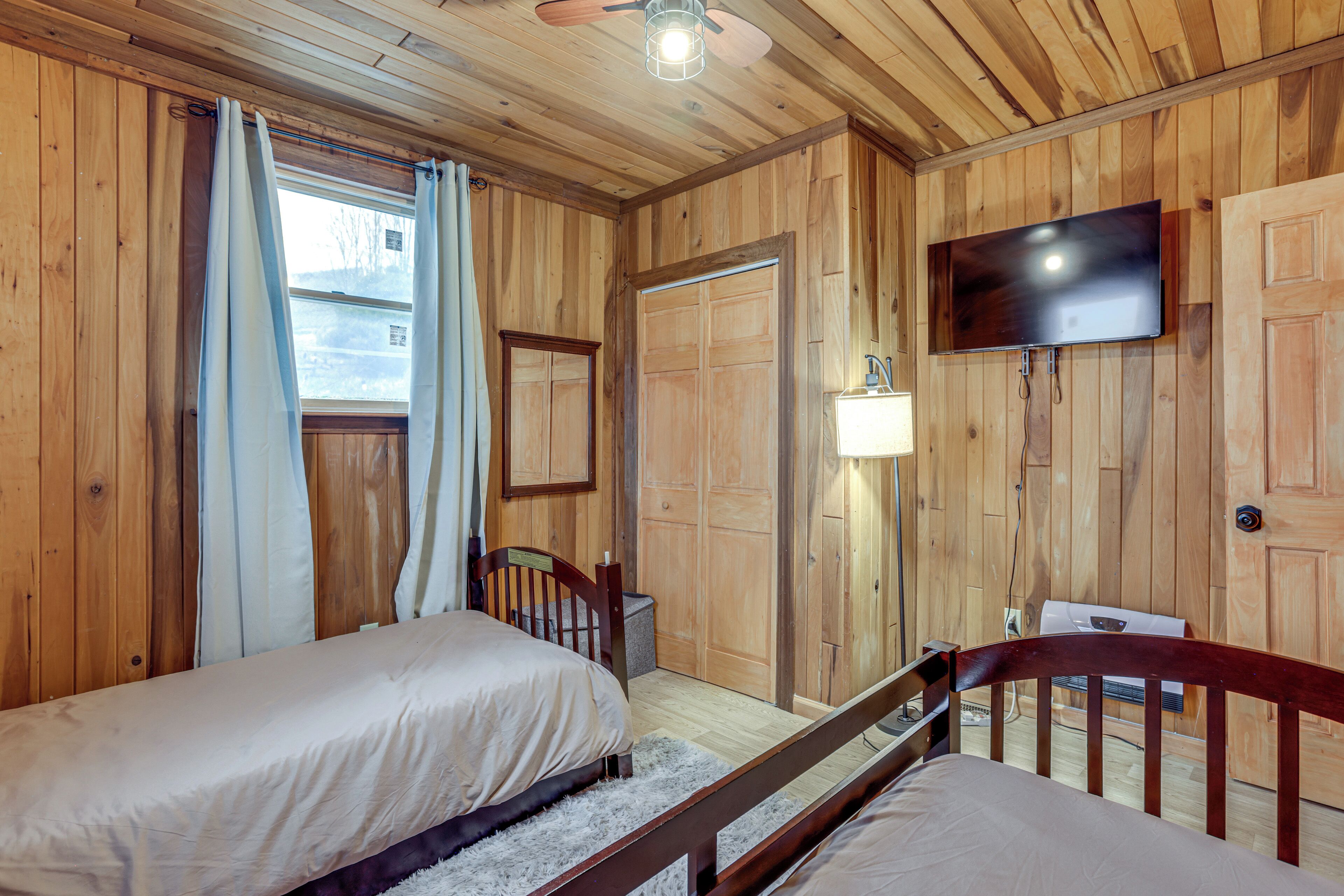 A wooden room with two beds, a TV, and a window with curtains.