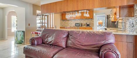 A living room with a leather sofa, wooden cabinets, and a kitchen area with a stone backsplash.