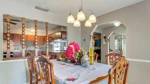 Un comedor con una mesa preparada para cuatro personas, rodeada de sillas de madera, un candelabro y un gran centro de mesa floral.