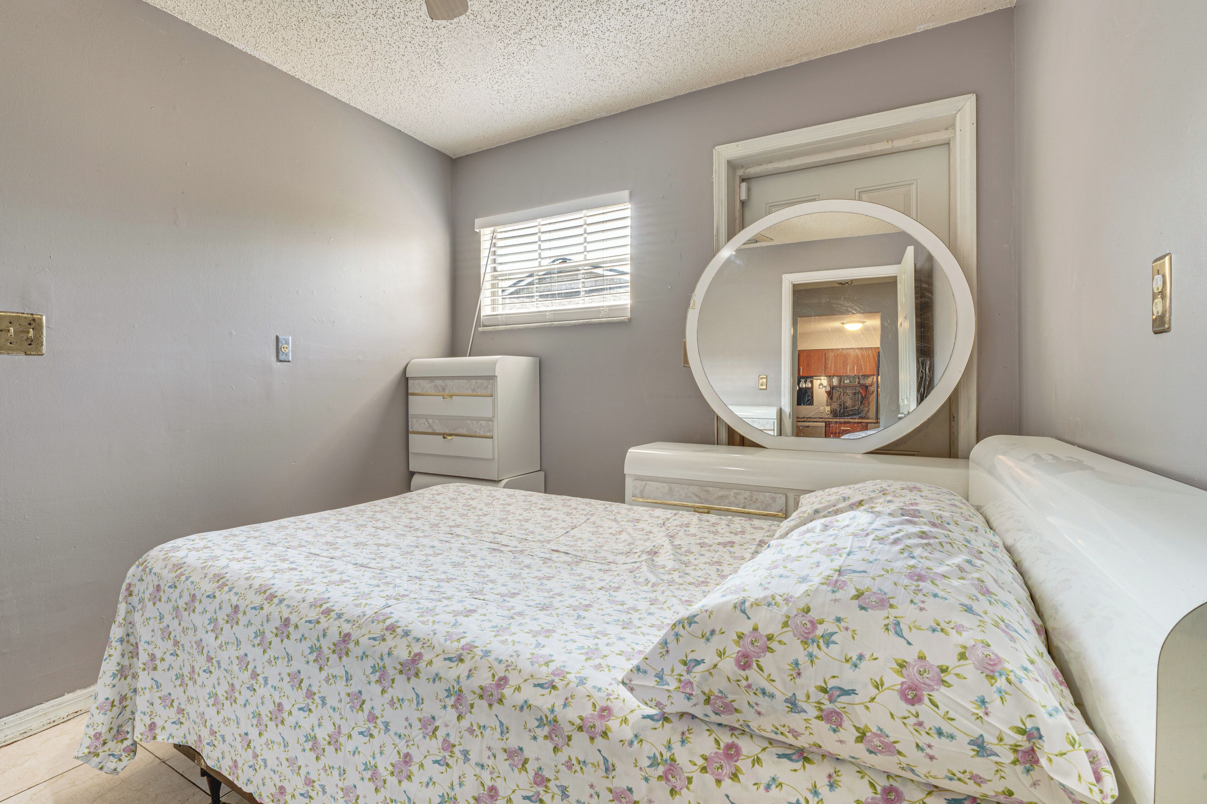A bedroom with a bed, a dresser, a mirror, and a window with blinds.