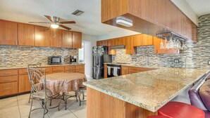 Una cocina con armarios de madera, encimera de granito, ventilador de techo y comedor con mesa y sillas.