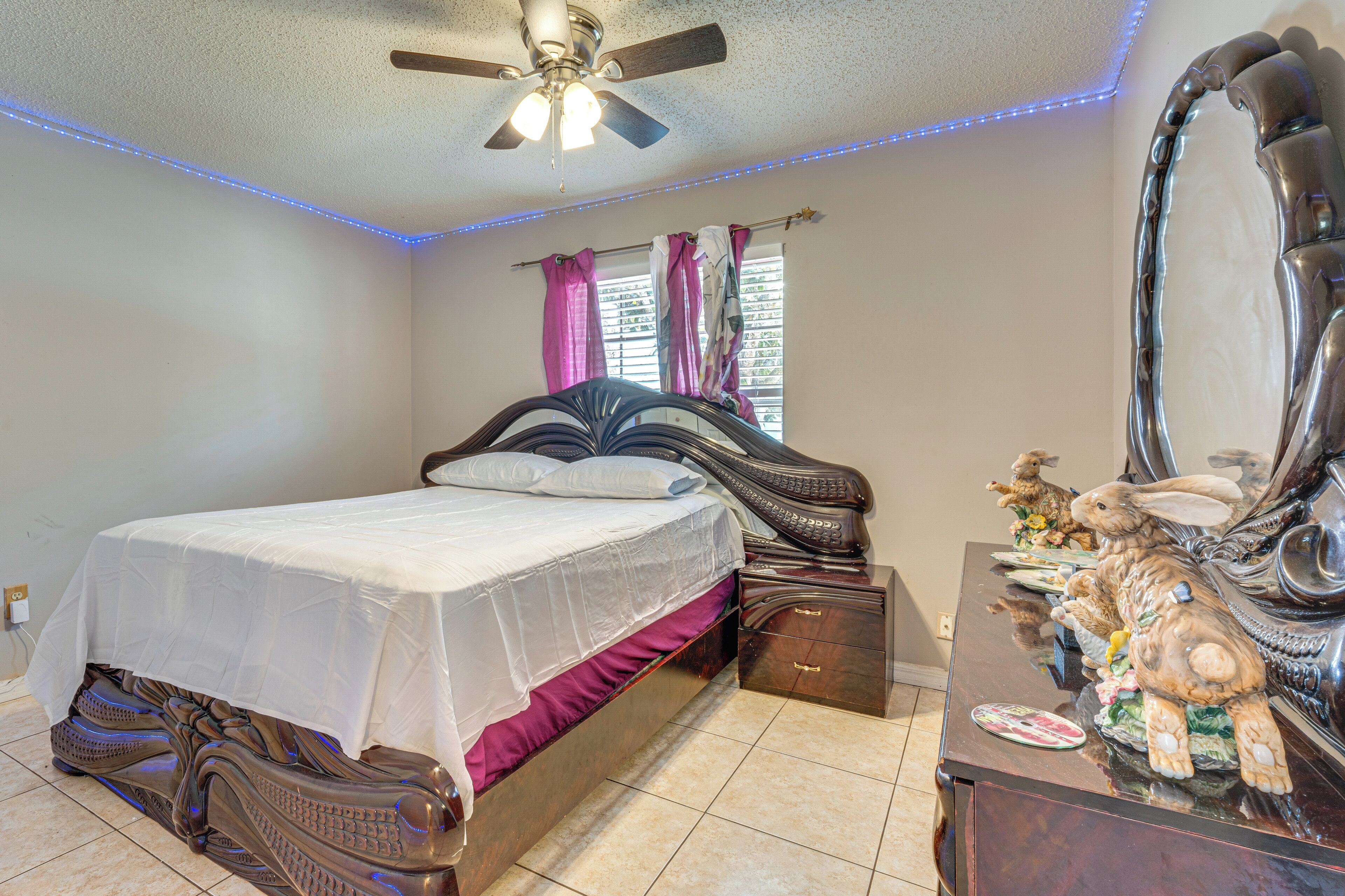A bedroom with a bed, a dresser, a ceiling fan, and a window with curtains.