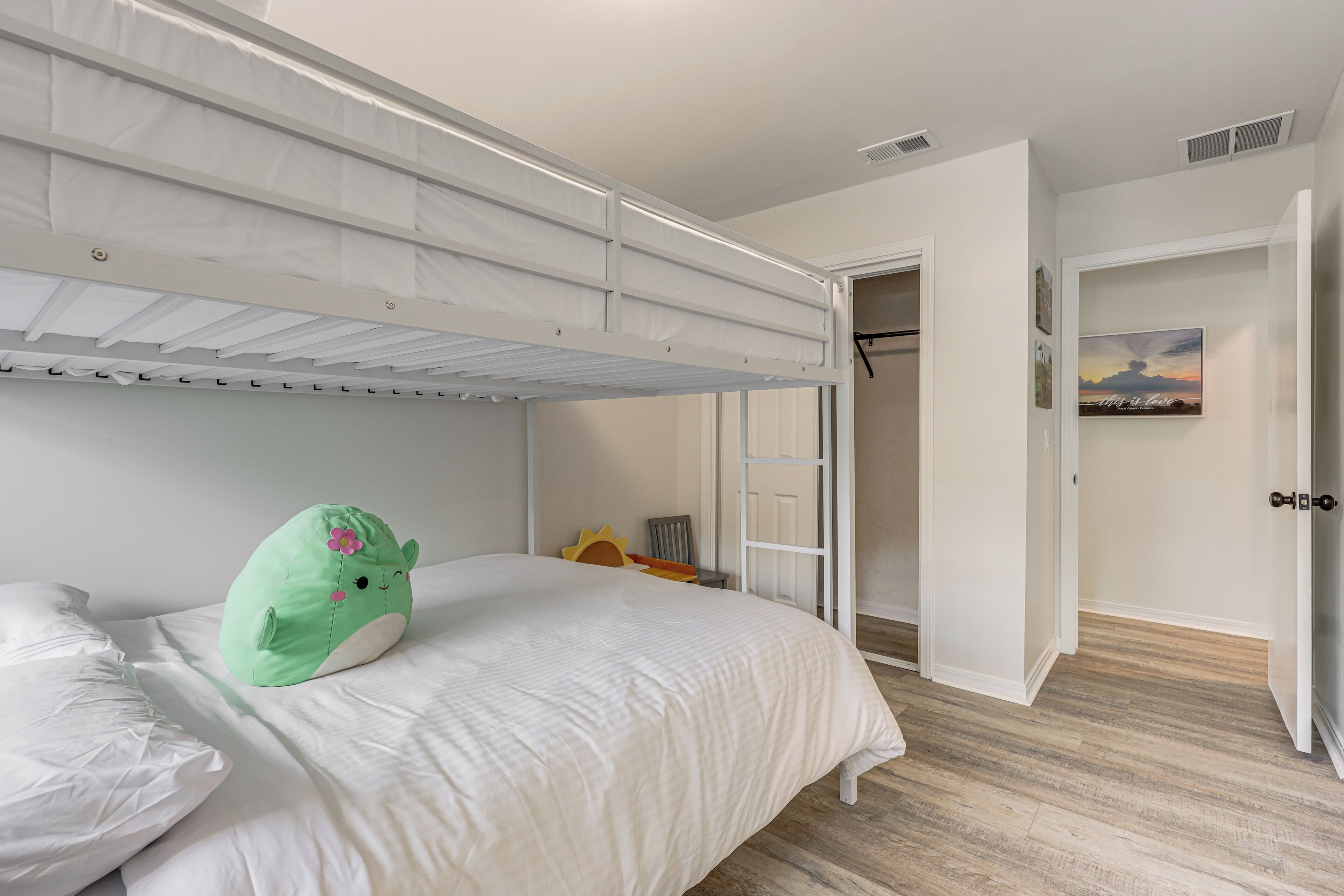 Ein Etagenbett mit einem grünen Plüschtier, einem weißen Kopfkissen und einer Tür zu einem Flur.
