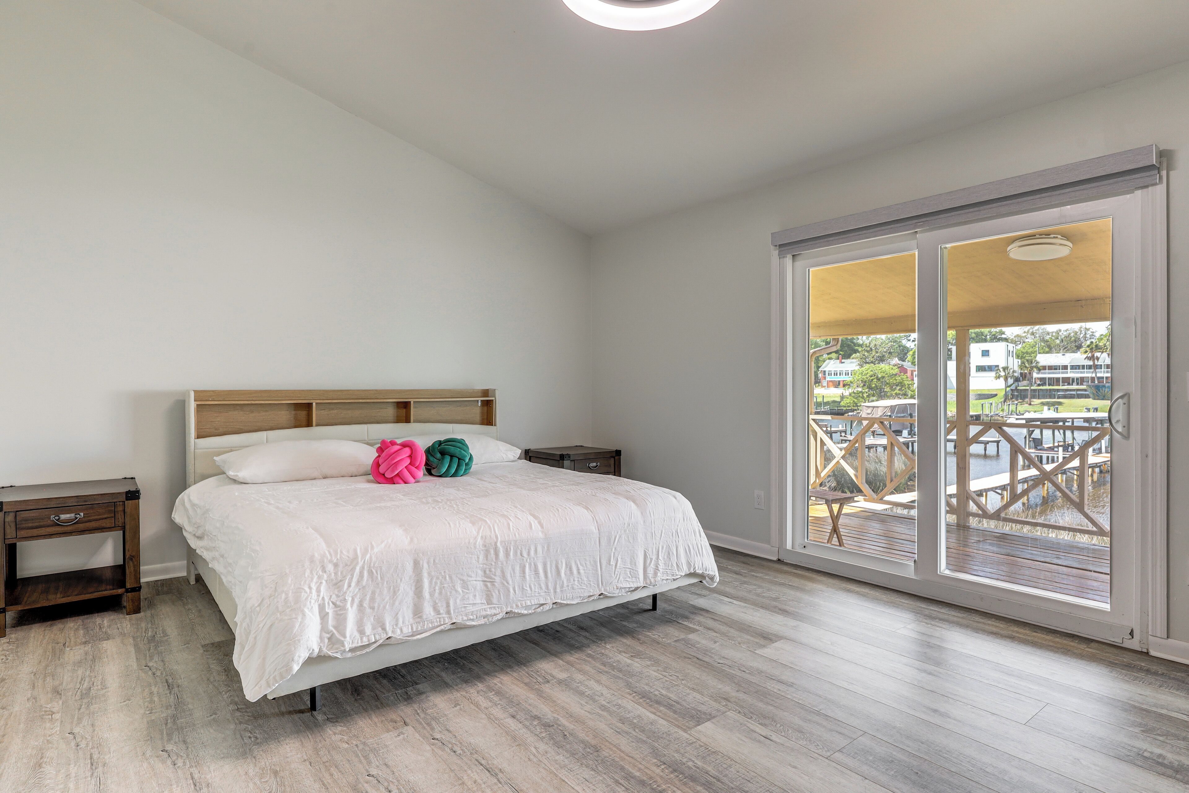 Un dormitorio con cama, mesita de noche, cabecero de madera y vistas a una terraza exterior a través de una puerta corrediza de vidrio.