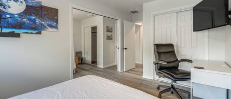Ein Schlafzimmer mit Bett, Schreibtisch, Stuhl, Deckenventilator und Wandfernseher.