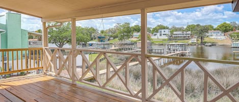 A wooden deck with a railing overlooking a body of water, docks, and buildings in the background.