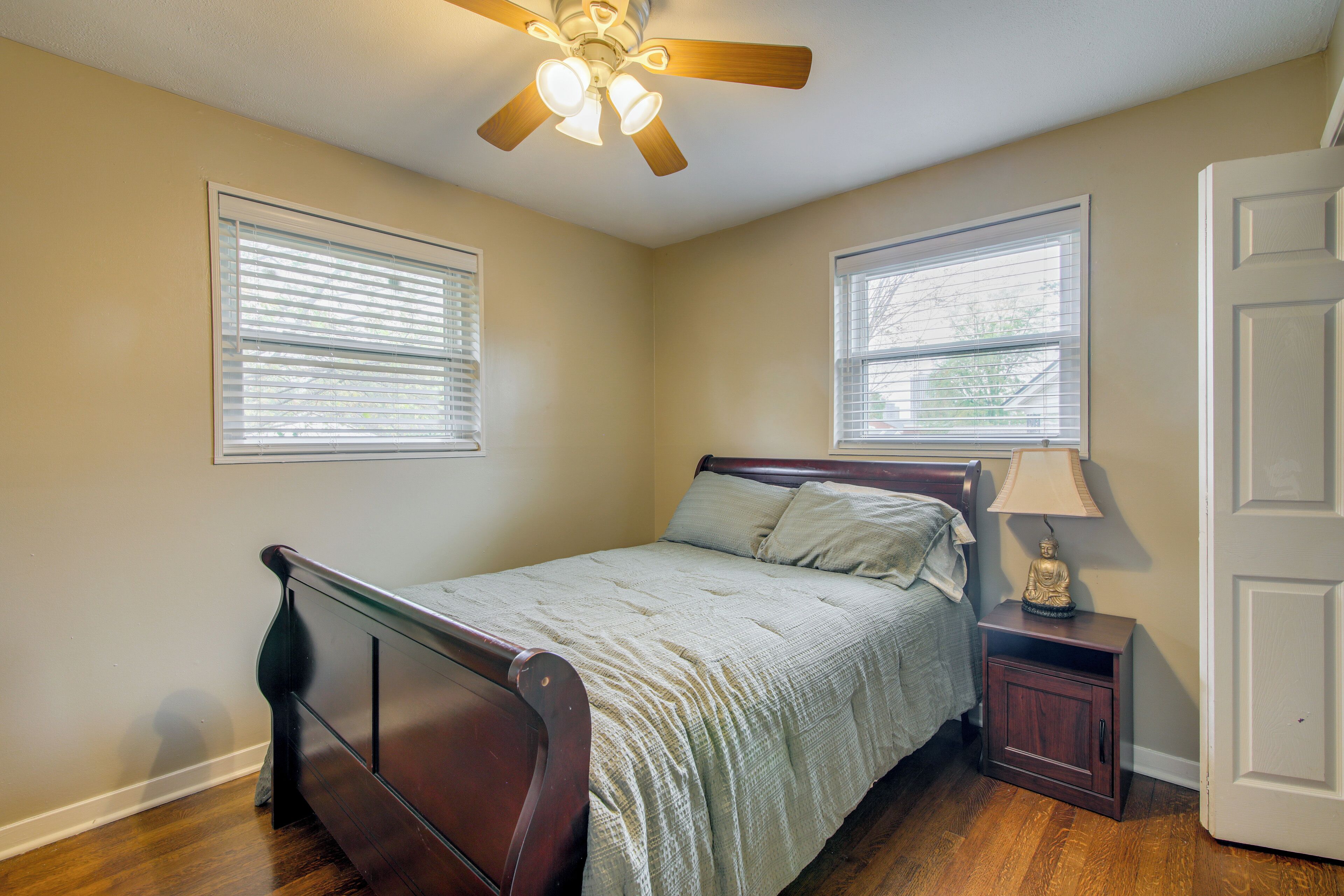A bedroom with a bed, nightstand, lamp, ceiling fan, and two windows.