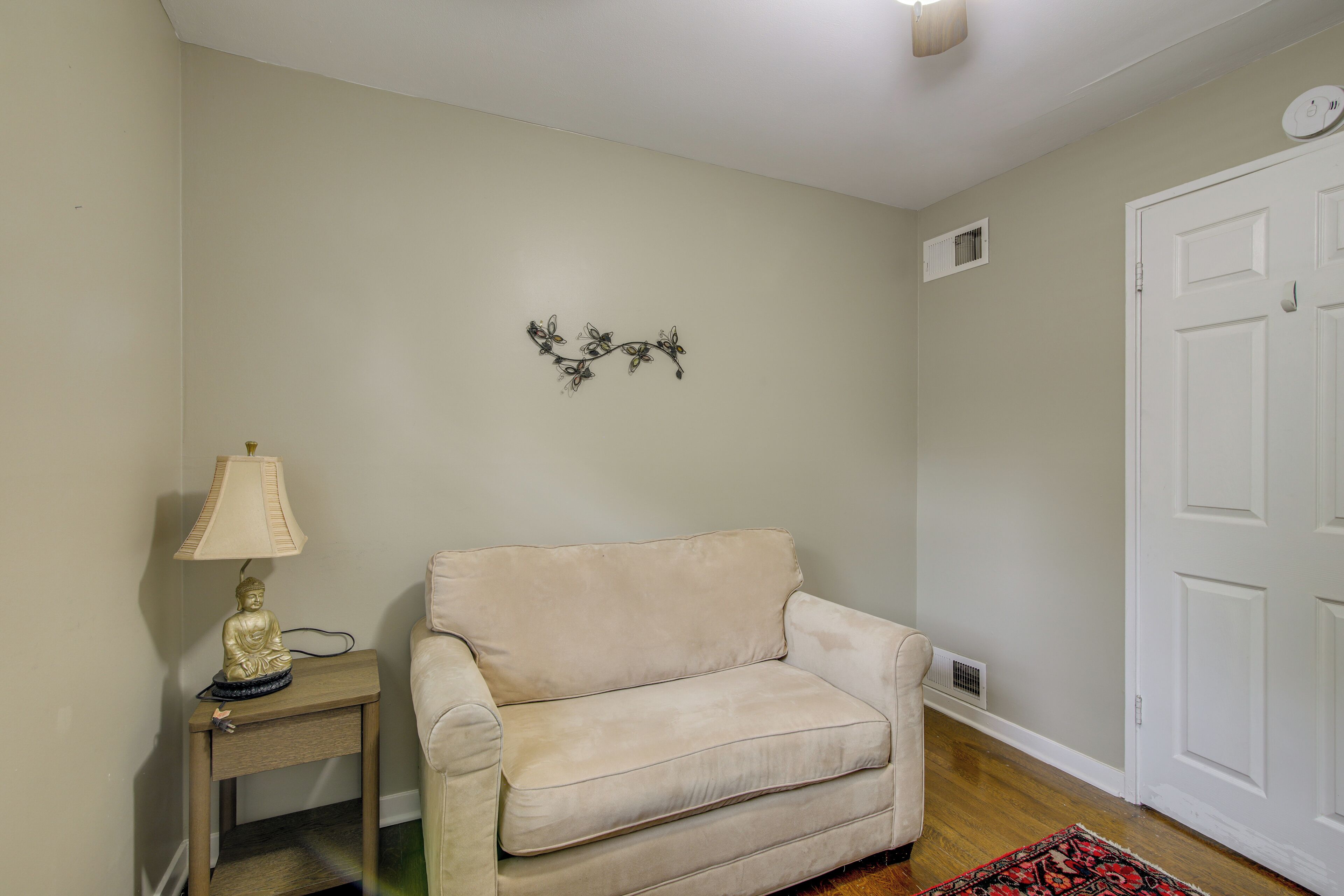 A beige sofa, a small table with a lamp, a decorative wall piece, and a white door.