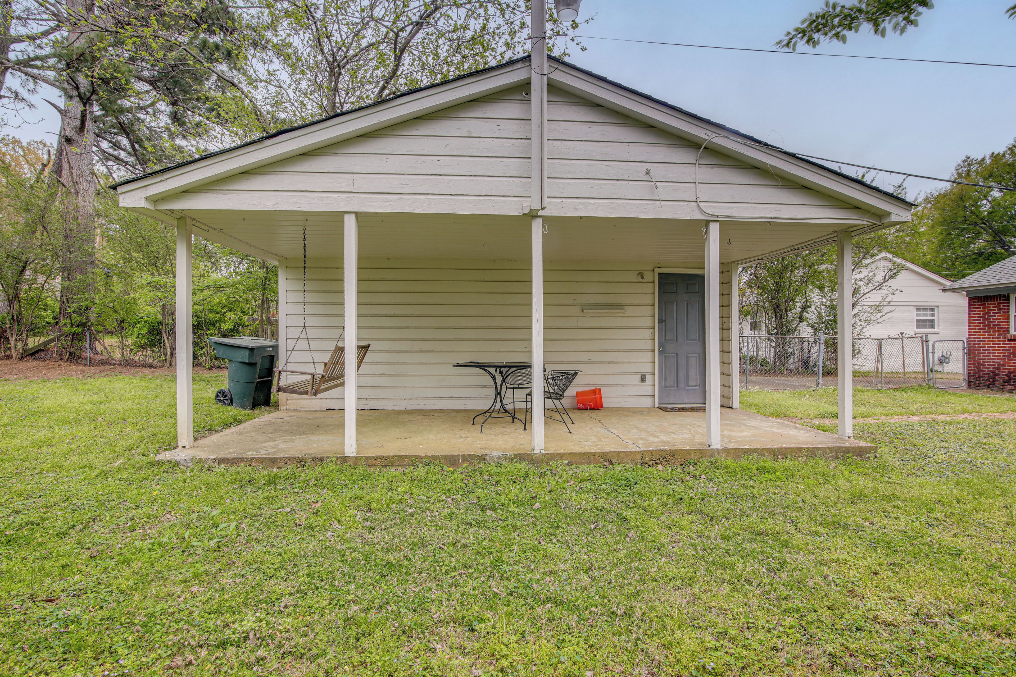 A covered porch with a table and chairs, a trash can, and a door.