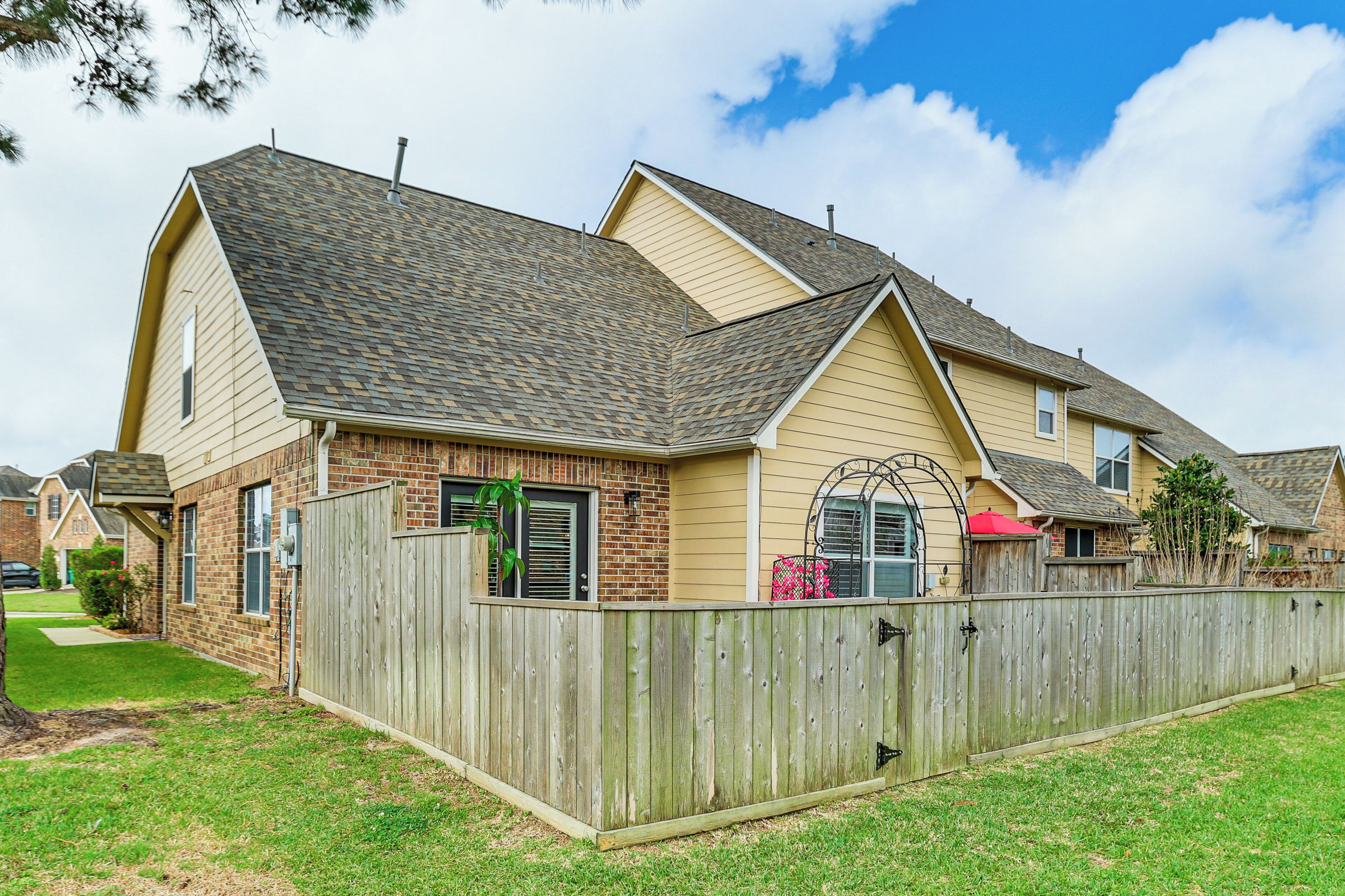 A residential house with a sloped roof, a wooden fence, and a brick foundation.