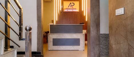 A reception desk with a wooden panel wall, a sign above it, and a staircase on the left.