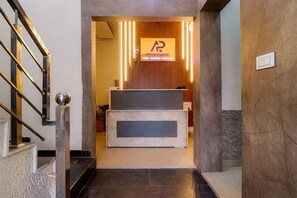 A reception desk with a wooden panel wall, a sign above it, and a staircase on the left. - Hotel Tanish (Haridwar)
