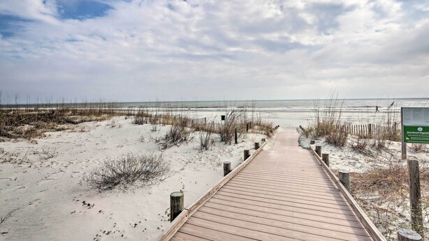 A wooden boardwalk leading to a beach with sand dunes and a cloudy sky.