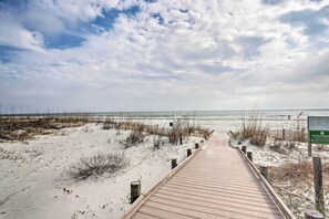 Een houten looppad naar een strand met duinen en een bewolkte lucht.