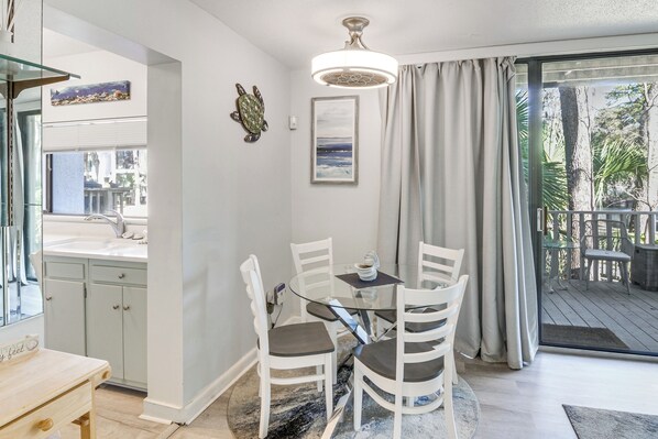 A dining area with a glass table and chairs, a ceiling light, a framed picture, and a view of the outdoors.