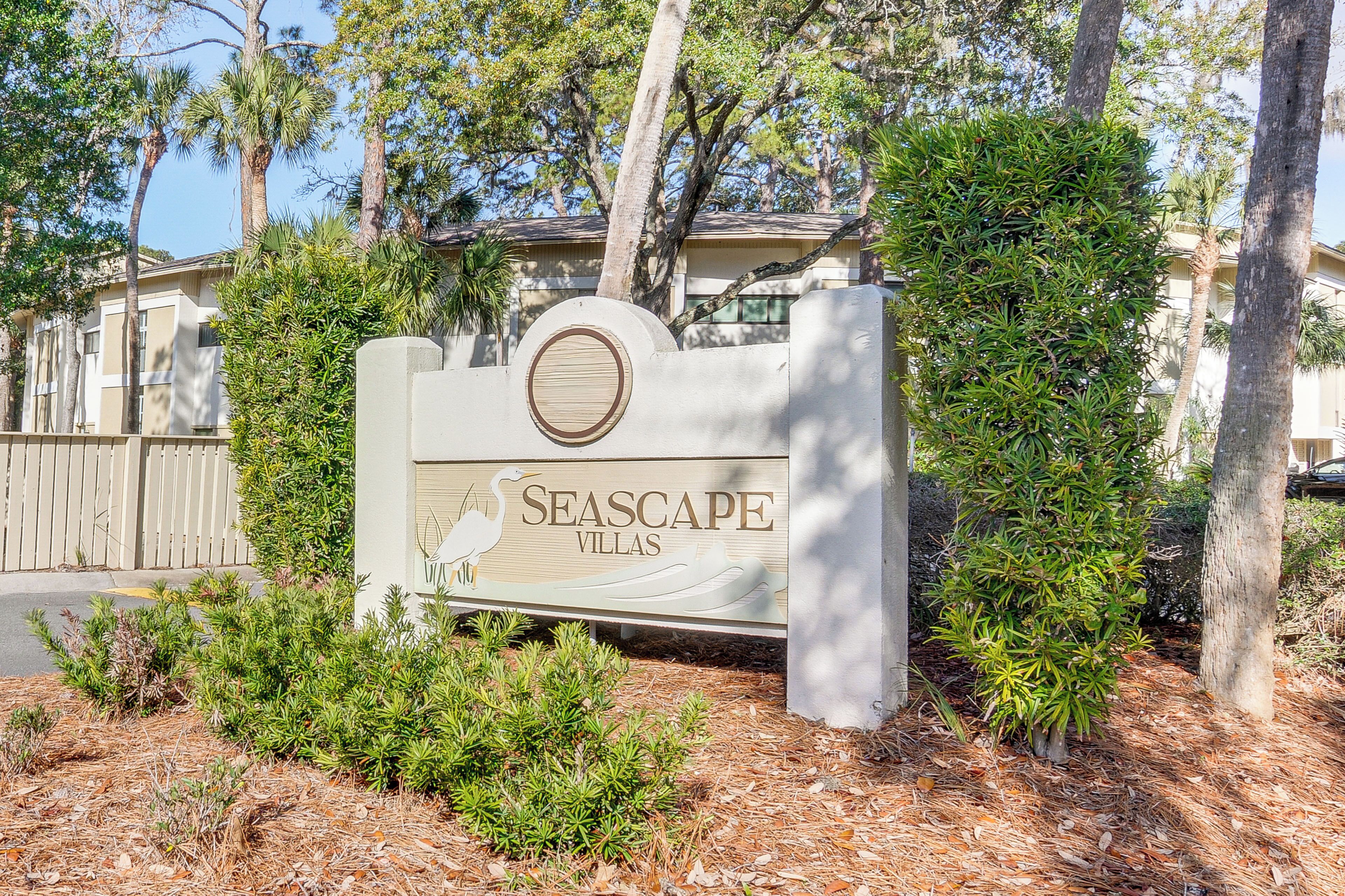 A sign for Seascape Villas with a circular emblem, surrounded by greenery and trees.