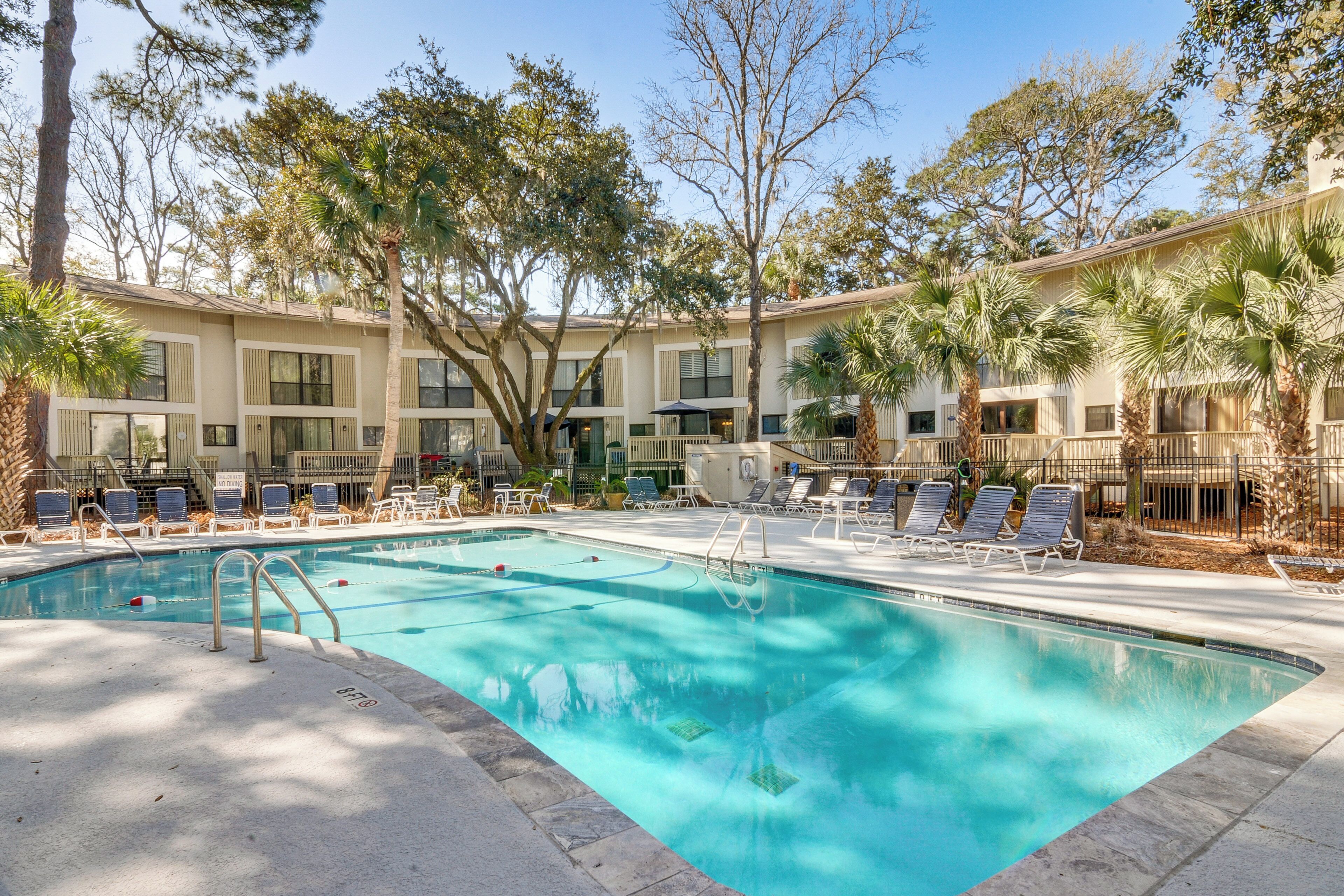 A swimming pool with lounge chairs, palm trees, and a building with multiple windows and balconies.