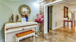 A piano with a bench, a mirror, and a vase with flowers in a room with a stone wall and a door leading to another room. - 2 Private Pools! 2-acre Retreat Near Dtwn Sarasota (Sarasota)