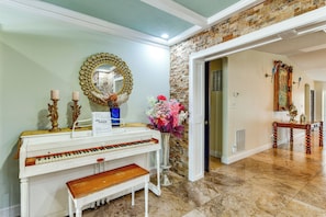 A piano with a bench, a mirror, and a vase with flowers in a room with a stone wall and a door leading to another room. - 2 Private Pools! 2-acre Retreat Near Dtwn Sarasota (Sarasota)