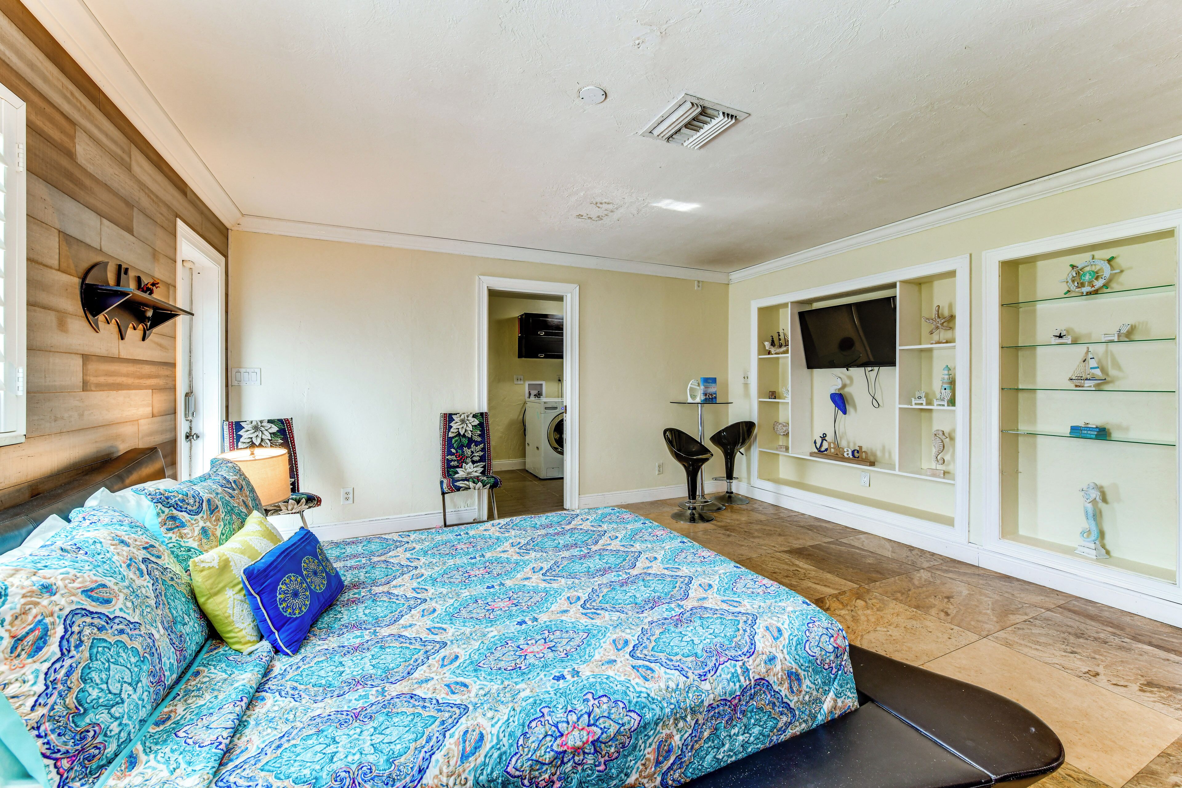 A bedroom with a bed, a chair, a TV, and a shelf with decorative items.