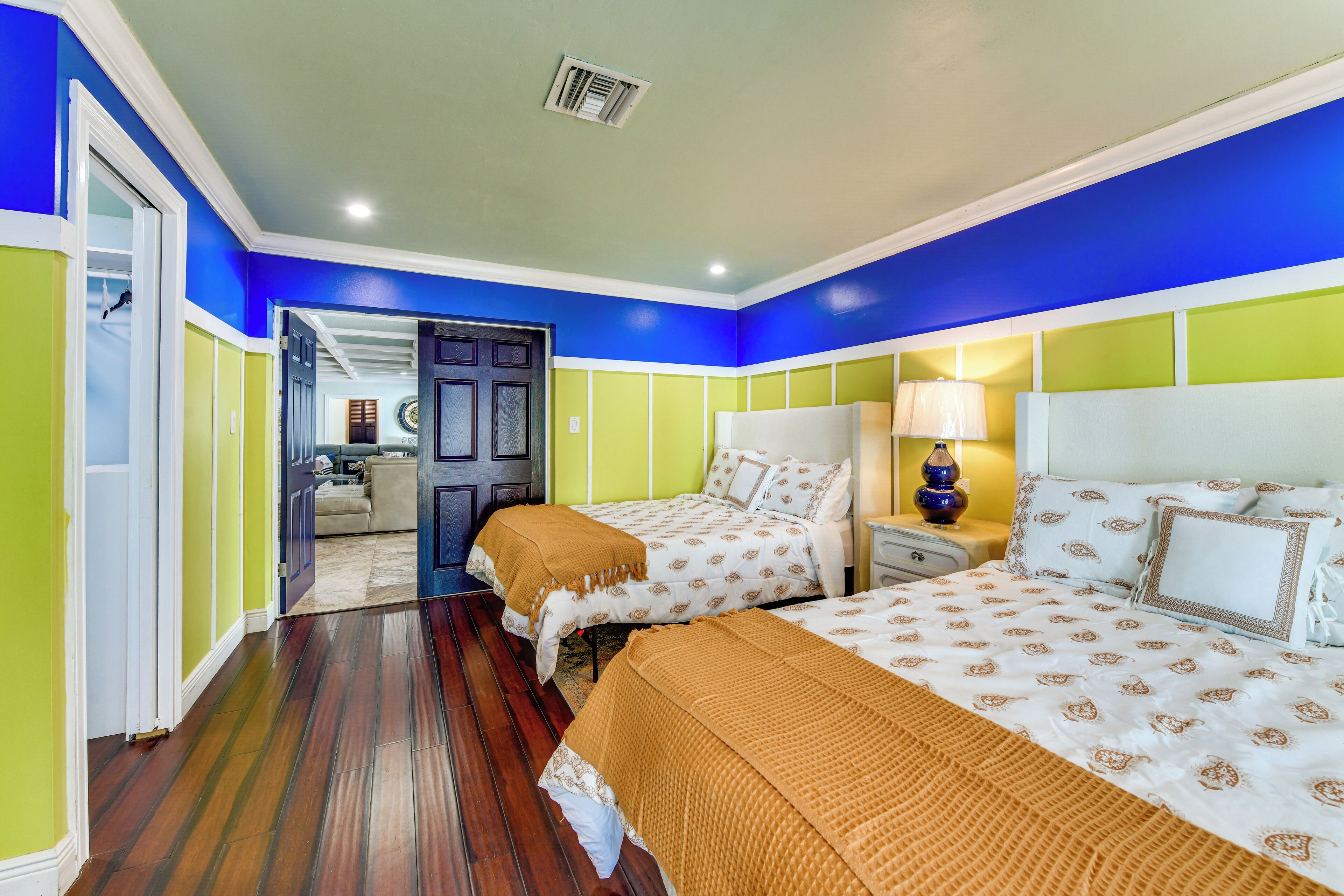 Habitación de hotel con dos camas, una mesita de noche, una lámpara y una puerta que da a otra habitación.