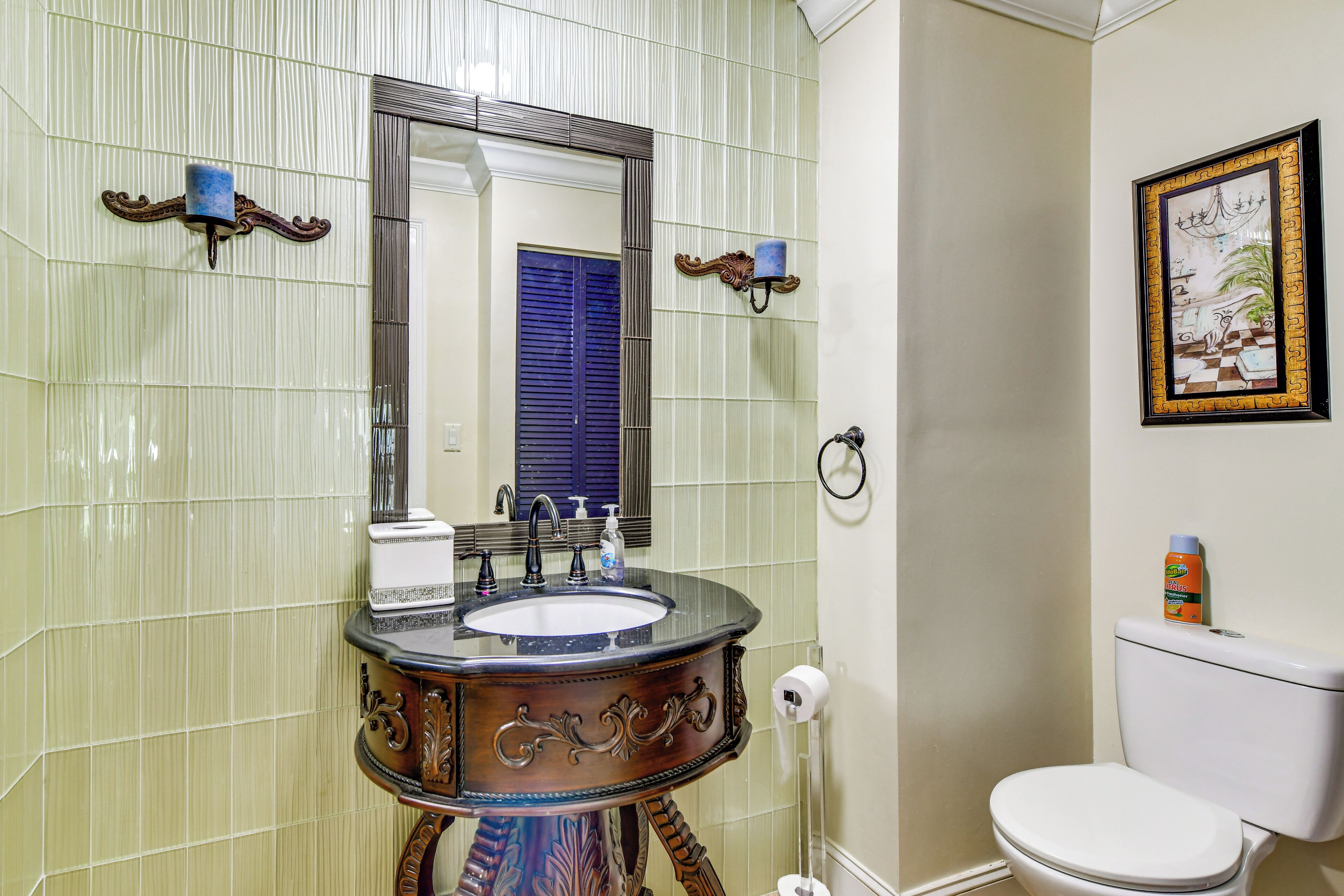 A bathroom with a vanity, sink, mirror, toilet, and a framed picture on the wall.