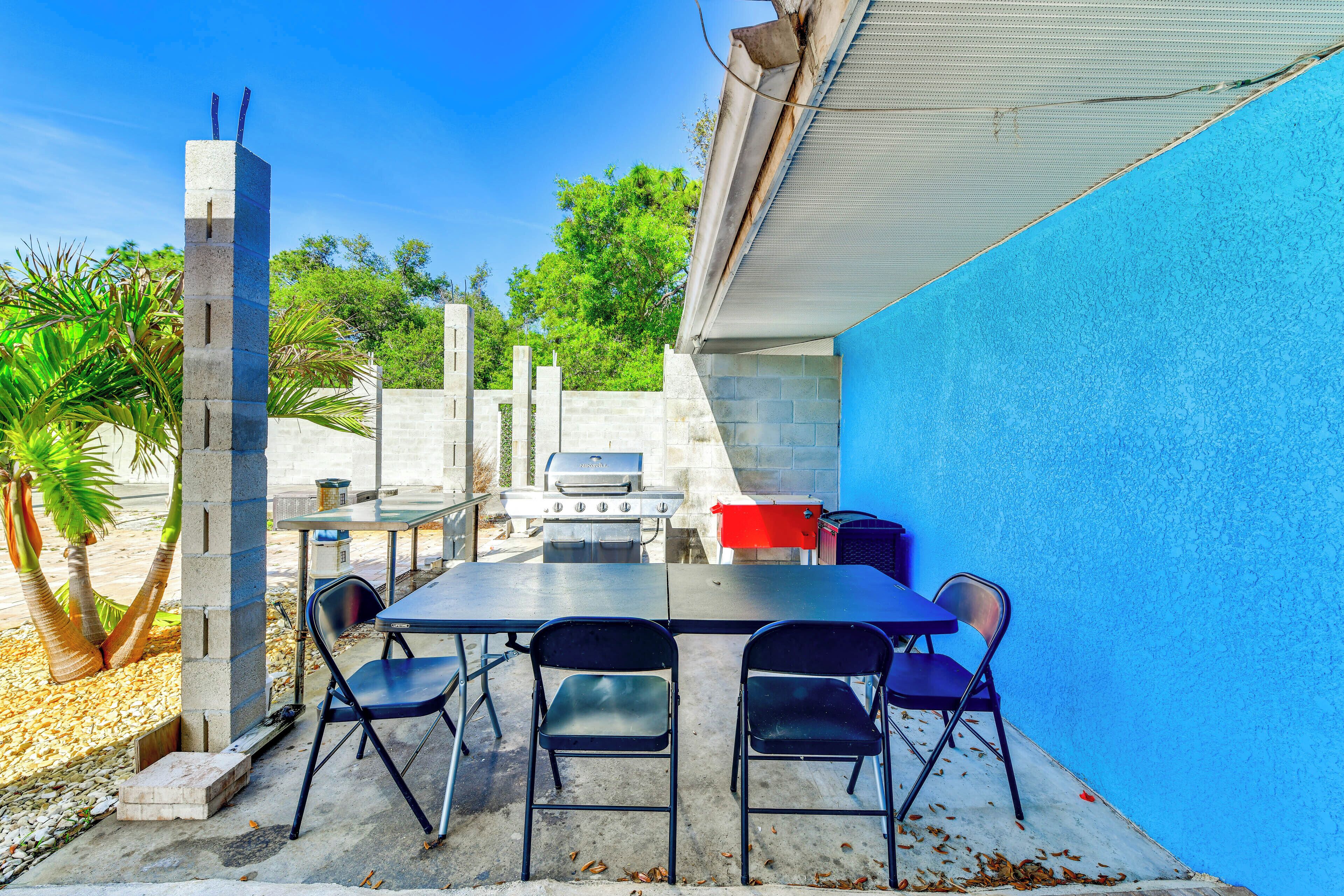 An outdoor patio with a table and chairs, a grill, and a blue wall.