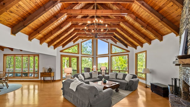 A spacious living room with a high wooden ceiling, large windows, and a stone fireplace. - DuPont Mountain Lodge: 28 Private Acres + Sauna (Cedar Mountain)
