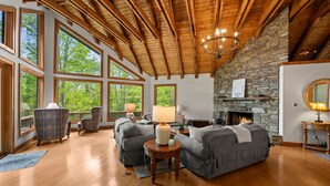 A spacious living room with a stone fireplace, large windows, and wooden beams. - DuPont Mountain Lodge: 28 Private Acres + Sauna (Cedar Mountain)