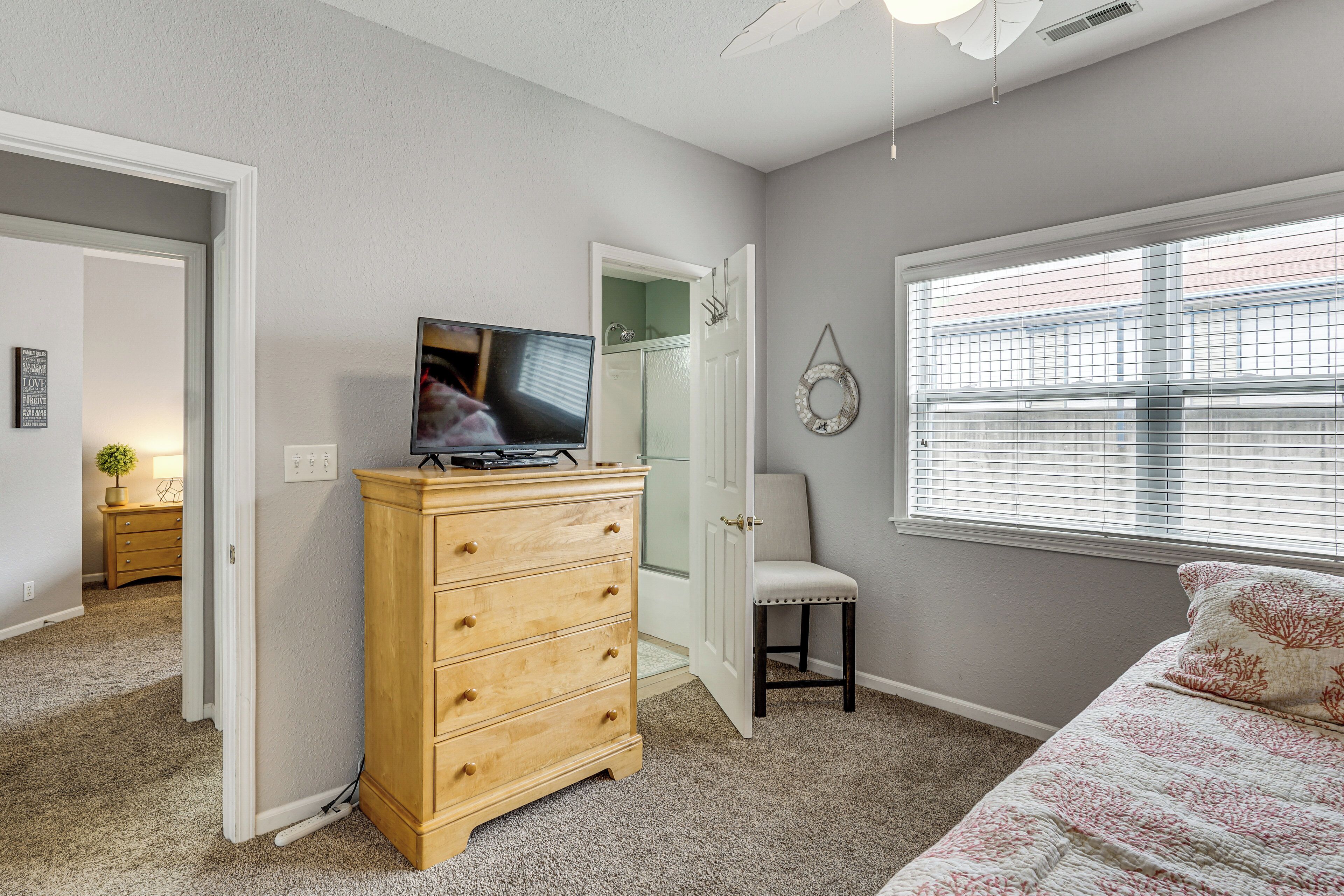 Une chambre à coucher comprenant un lit, une commode, un téléviseur, une chaise et une fenêtre avec des stores.