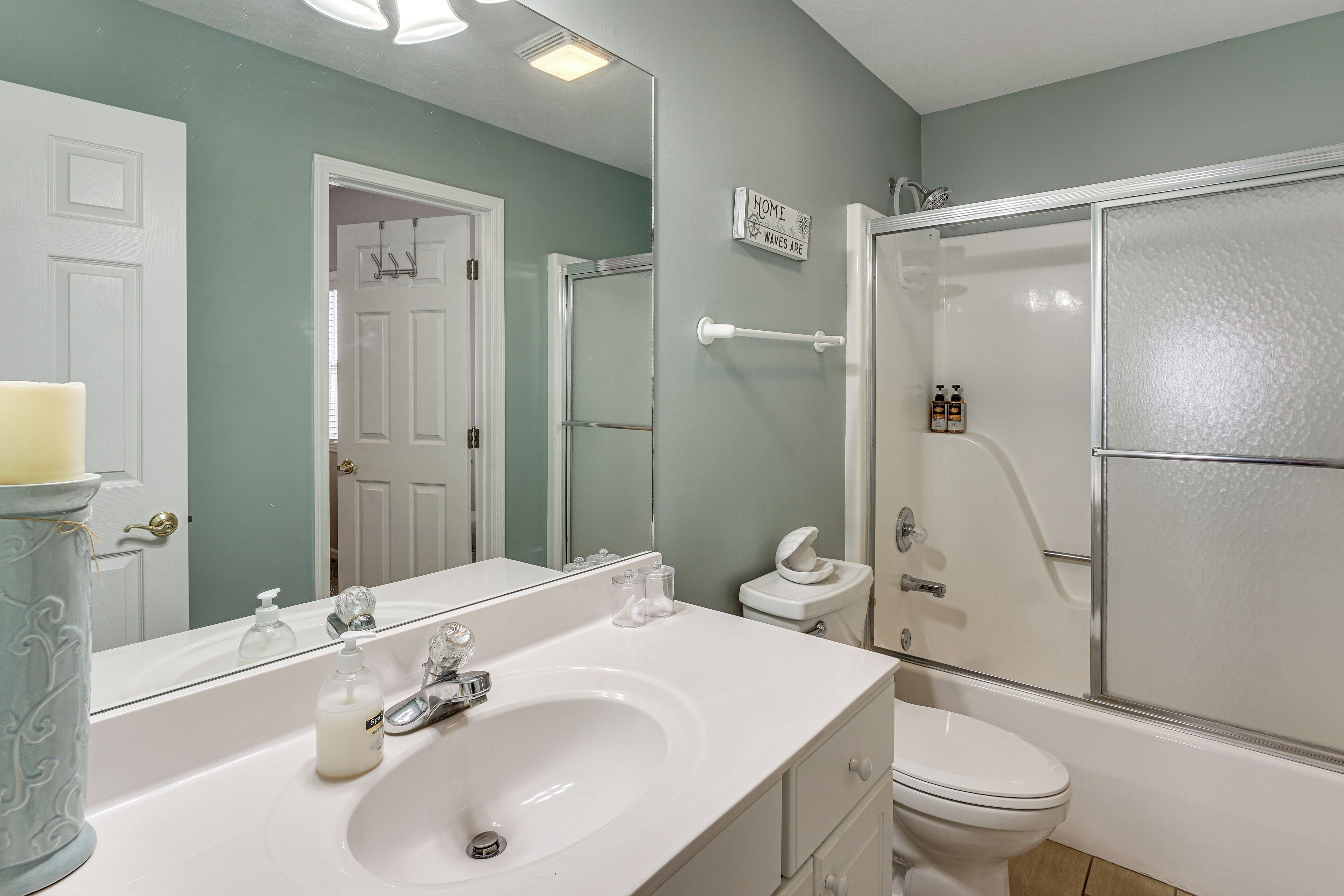 Une salle de bain avec un lavabo blanc, un miroir et des toilettes, un espace douche et une enseigne indiquant « HOME WAVE LOB ».