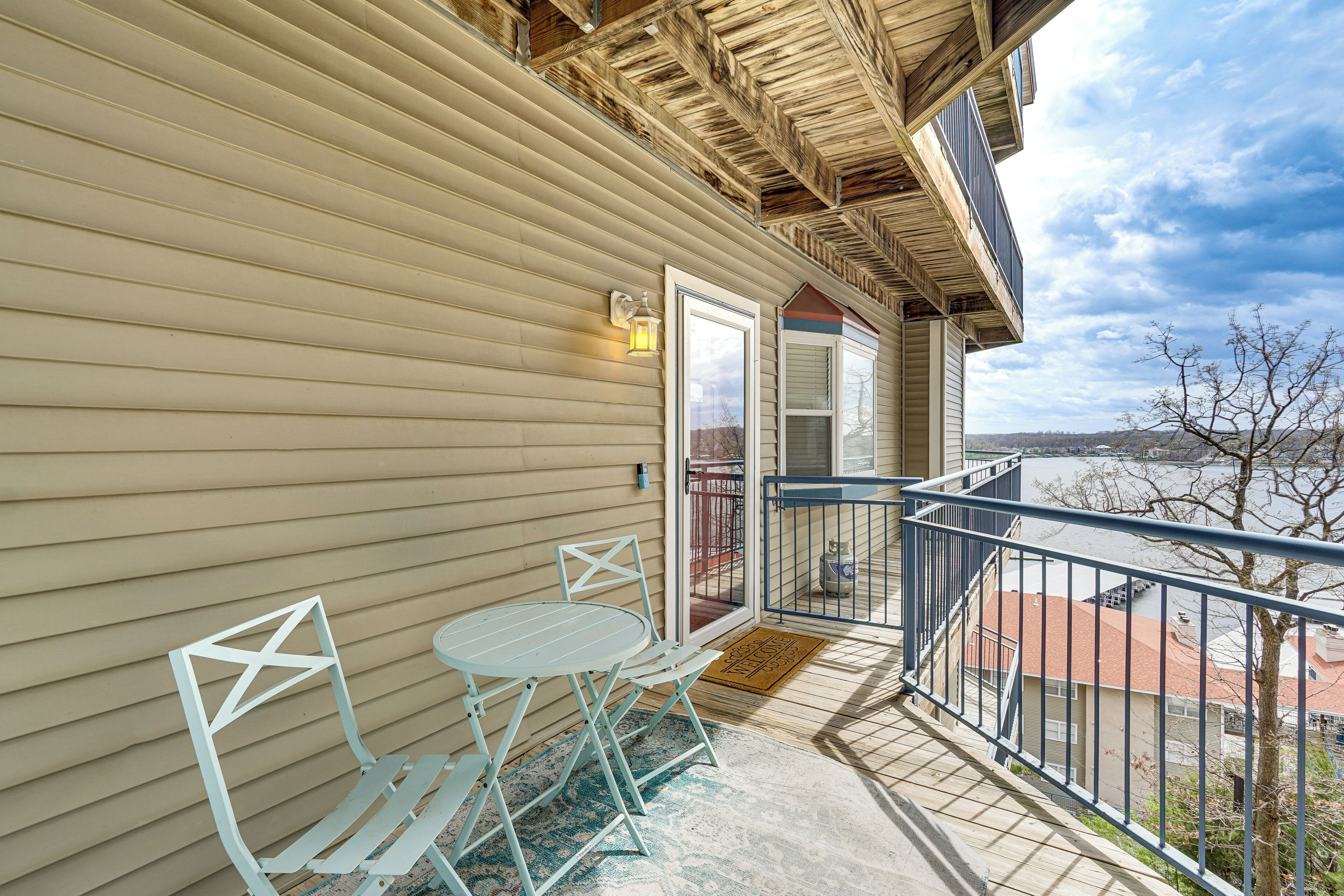 A balcony with a table and chairs, a railing, and a view of a river and buildings.