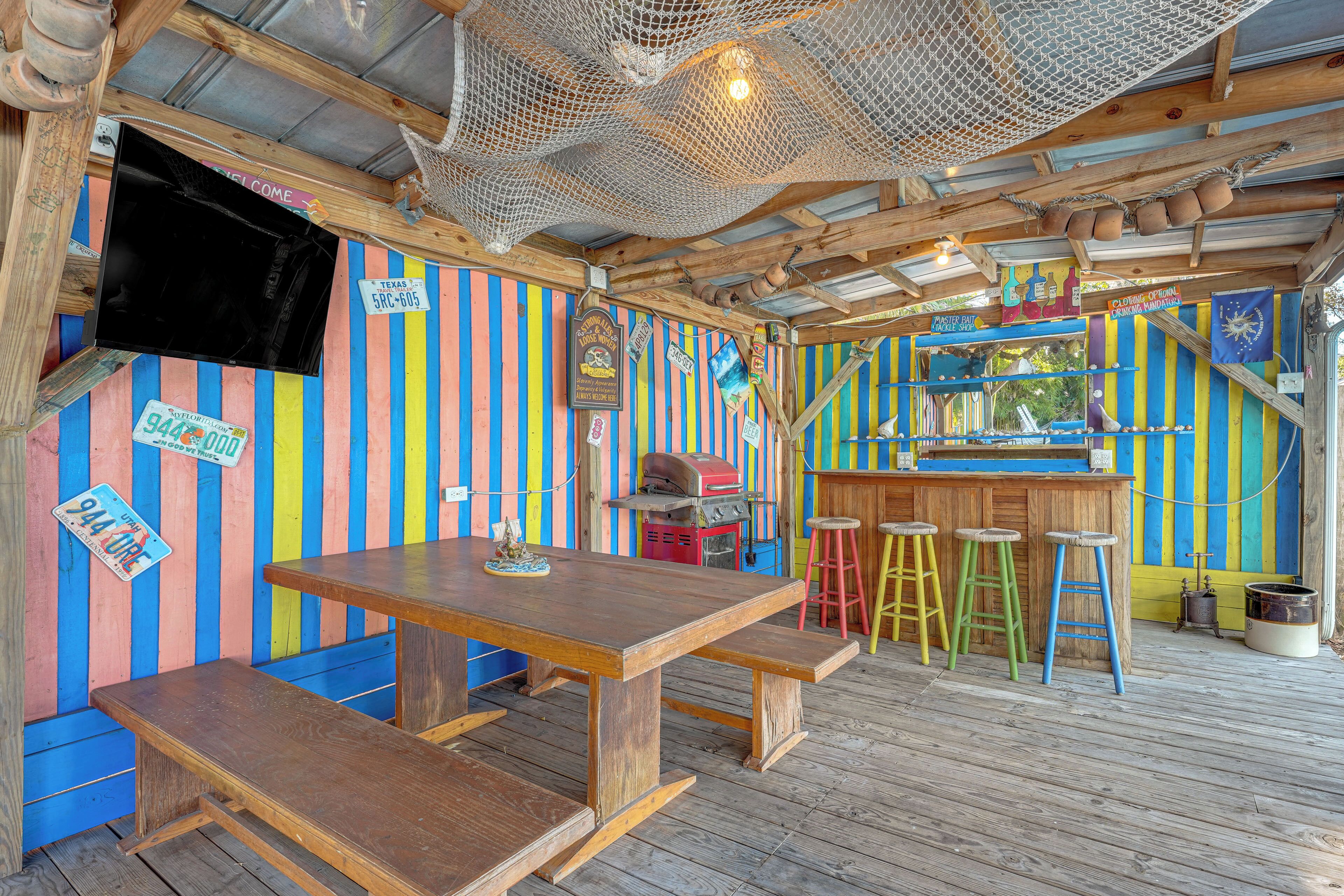 A colorful, rustic bar area with a wooden table and stools, a grill, and striped walls.