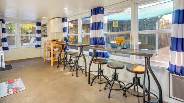 A kitchen with a bar area, large windows with curtains, and a view of the outside. - Sun & Sand in St Pete! Family Home w/ Tiki Bar (St. Petersburg)