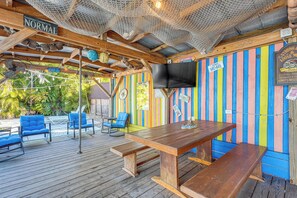 Una terraza de madera con una mesa y sillas, un televisor montado en la pared y un llamativo muro a rayas.
