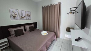 A hotel room with a bed, a TV, a curtain, and artwork on the wall.
