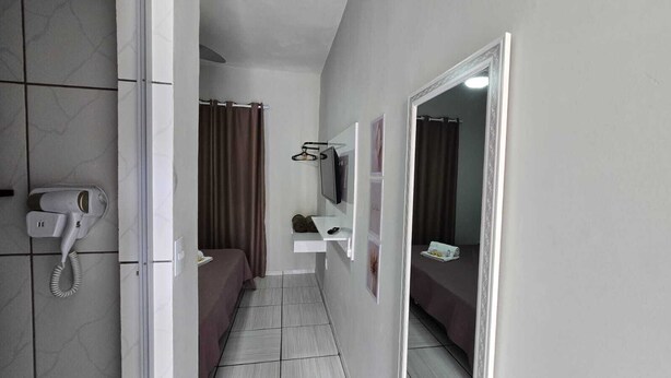 A narrow hotel corridor with a hairdryer, a mirror, and a bed with a brown cover.