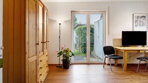 Ein Zimmer mit einem Holzschrank, einem Schreibtisch mit Stuhl, einer Topfpflanze und einem Fernseher.