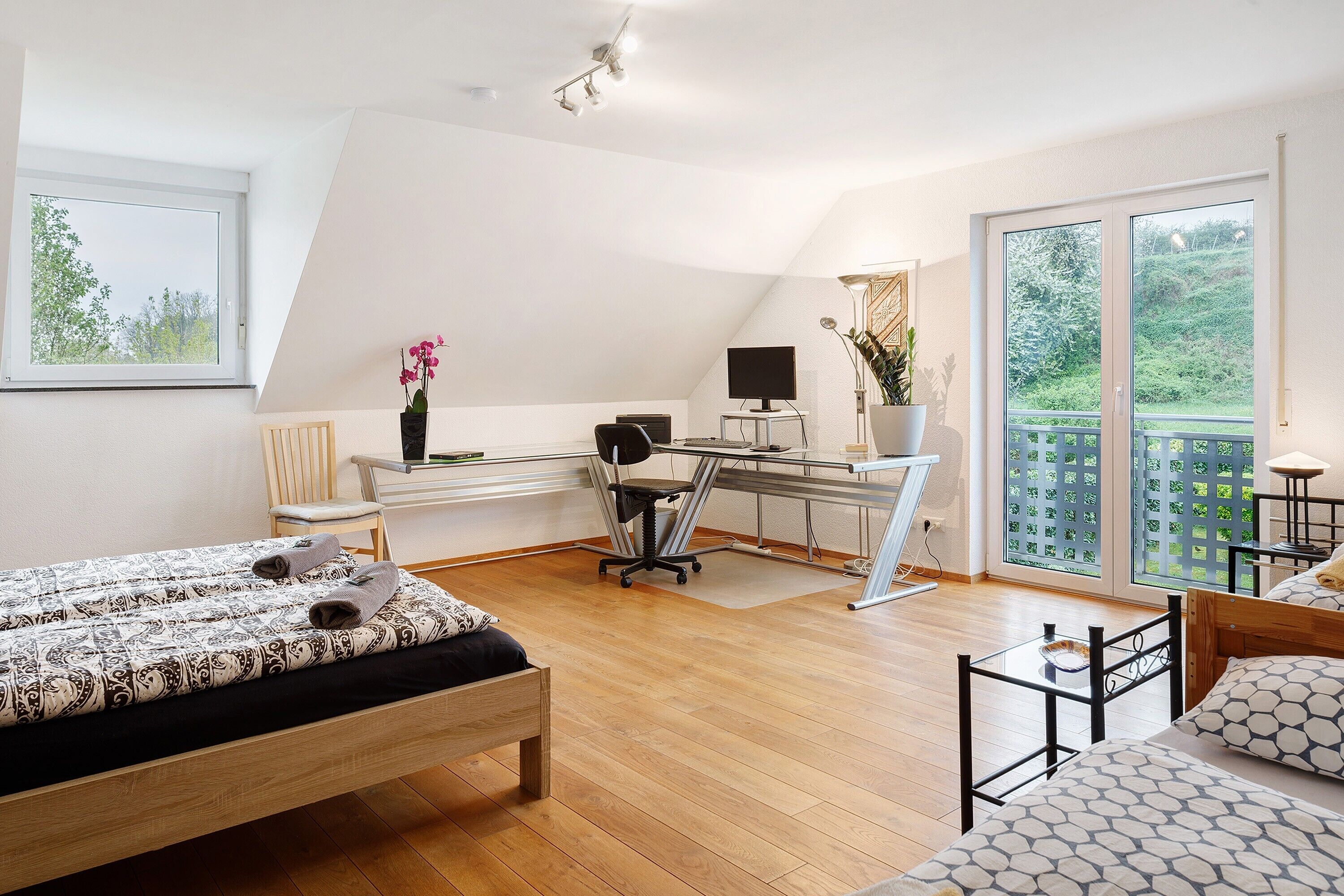 A bedroom with a bed, a desk, a computer, and a balcony with a view.