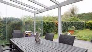 Eine Außenpatio mit Tisch und Stühlen, einer Glasveranda und Blick auf einen Garten.